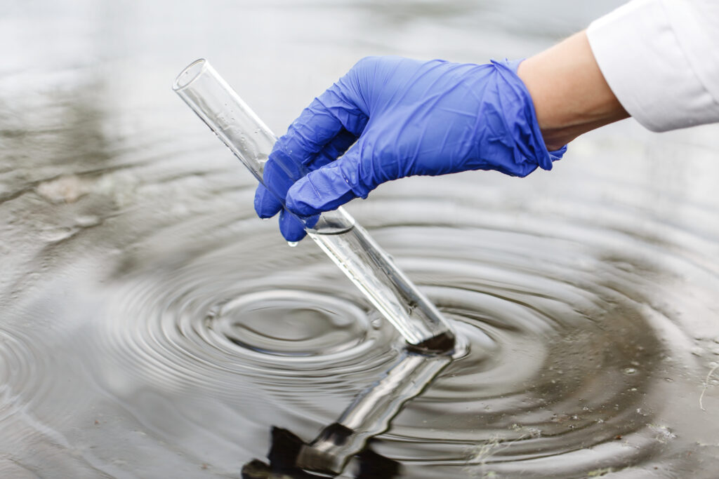 Researcher holds a test tube with water in a hand in blue glove | NewRoad